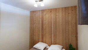 Une chambre avec deux lits, des murs lambrissés, un luminaire au plafond et une plante en pot.