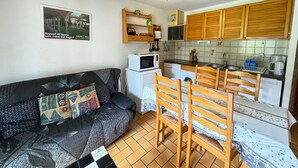 Ett kompakt bostadsutrymme med en soffa, trästolar, ett köksområde med träskåp, en mikrovågsugn och en tvättmaskin.