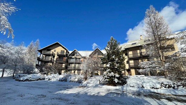 En snötäckt semesteranläggning med flera byggnader, inklusive ett hotell med balkonger och en skidstuga.