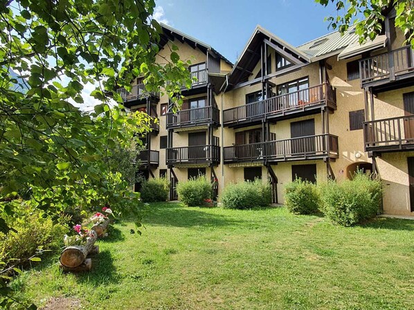 Un immeuble à plusieurs étages doté de balcons, entouré de verdure et d’une pelouse bien entretenue.