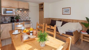 Een gezellige keuken met houten kasten, een eettafel gedekt met ontbijtartikelen en een houten bank met een deken.