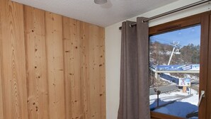 Een kamer met houten lambrisering, een bed met witte lakens en een raam met uitzicht op een skilift en een besneeerd landschap.