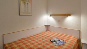 A small, single-bed room with a plaid bedspread, a framed picture on the wall, and a shelf with a lamp. - Ski-in apartment, 5 pers, pets allowed (Belle Plagne)