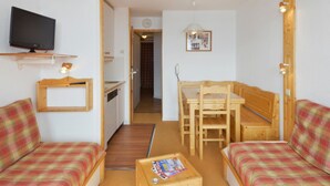 A compact room with a kitchenette, a television, a dining table with chairs, and two plaid-patterned sofas. - Ski-in apartment, 5 pers, pets allowed (Belle Plagne)