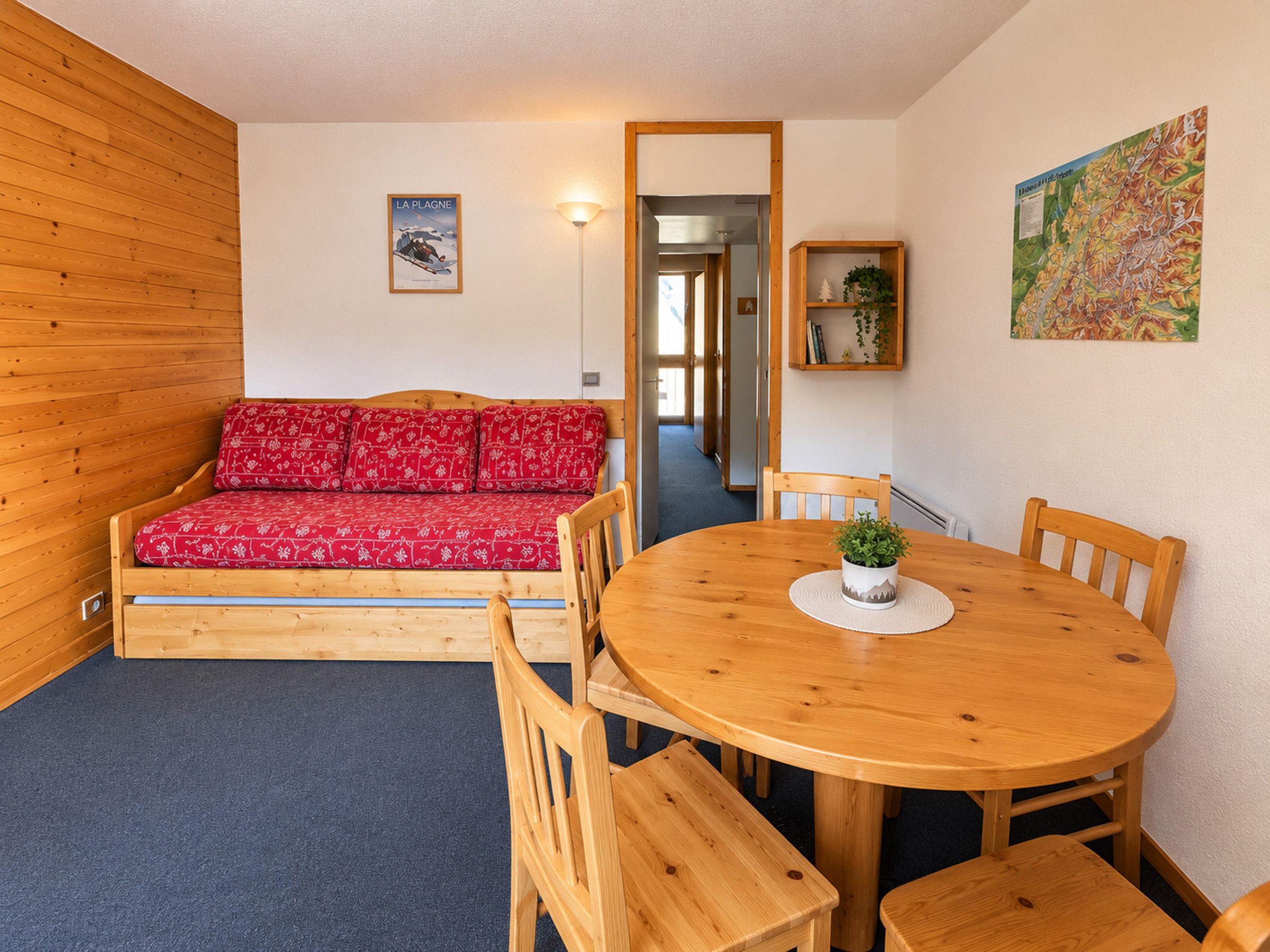 A cozy room with a wooden sofa, a round wooden table with chairs, and a small potted plant.