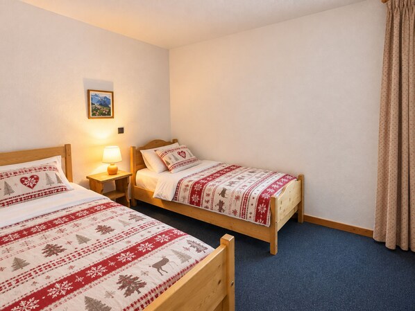 A room with two wooden beds, each with a patterned bedspread and pillows, a bedside table with a lamp, and a framed picture on the wall.