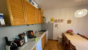 Une cuisine compacte avec des meubles en bois, un plan de travail blanc, un évier et un coin repas comprenant une table et des chaises.