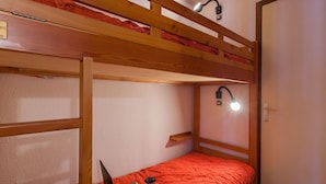 Une chambre avec un lit superposé, un ordinateur portable posé sur le lit du bas, une lampe de bureau et une porte.