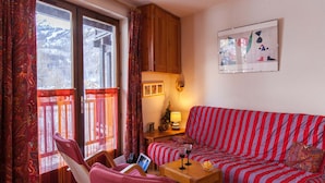 Un salon chaleureux avec un canapé à rayures, une table basse en bois et un fauteuil. On y trouve une fenêtre avec des rideaux, une petite table avec une lampe et un tableau encadré au mur.