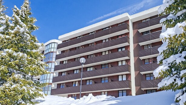 A multi-story building with balconies, surrounded by snow-covered trees.