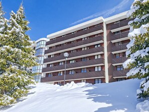 A multi-story building with balconies, surrounded by snow-covered trees.