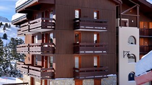 Un immeuble à plusieurs étages doté de balcons en bois, d’une fondation en pierre et, en arrière-plan, d’une piste de ski.
