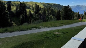 Une route asphaltée, avec une zone herbeuse d’un côté et une colline boisée en arrière-plan.
