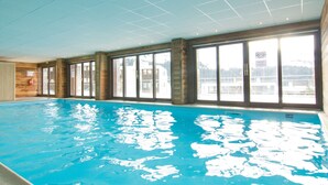 An indoor swimming pool with clear blue water, large windows, and a view of the outside. - Ski-in apartment with pool and parking (Flaine)