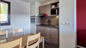 Kompakti keittiö, jossa on ruokailutila, pöytä ja tuolit, mikroaaltouuni, uuni ja kaapit.