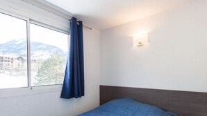 Una camera da letto con un letto, una finestra con tende, un comodino e una lampada a muro.