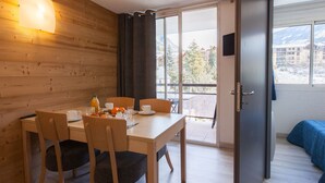 Una camera moderna con una parete in legno, un tavolo da pranzo con sedie, un balcone con vista su edifici e alberi e un letto con copriletto blu.