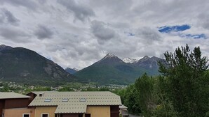 A building with multiple floors and a flat roof, surrounded by lush greenery and mountains in the background. - Apartment near lifts, free wifi, pets allowed (Briançon)