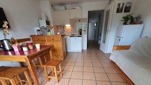 A compact kitchen with wooden cabinets, a dining table with chairs, a refrigerator, and a sofa in a living area. - Apartment near lifts, free wifi, pets allowed (Briançon)