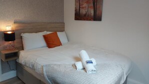 A neatly made bed with white and orange pillows, a rolled towel, and a painting of a forest scene on the wall. - 7 Eyre Square Lane (Galway)
