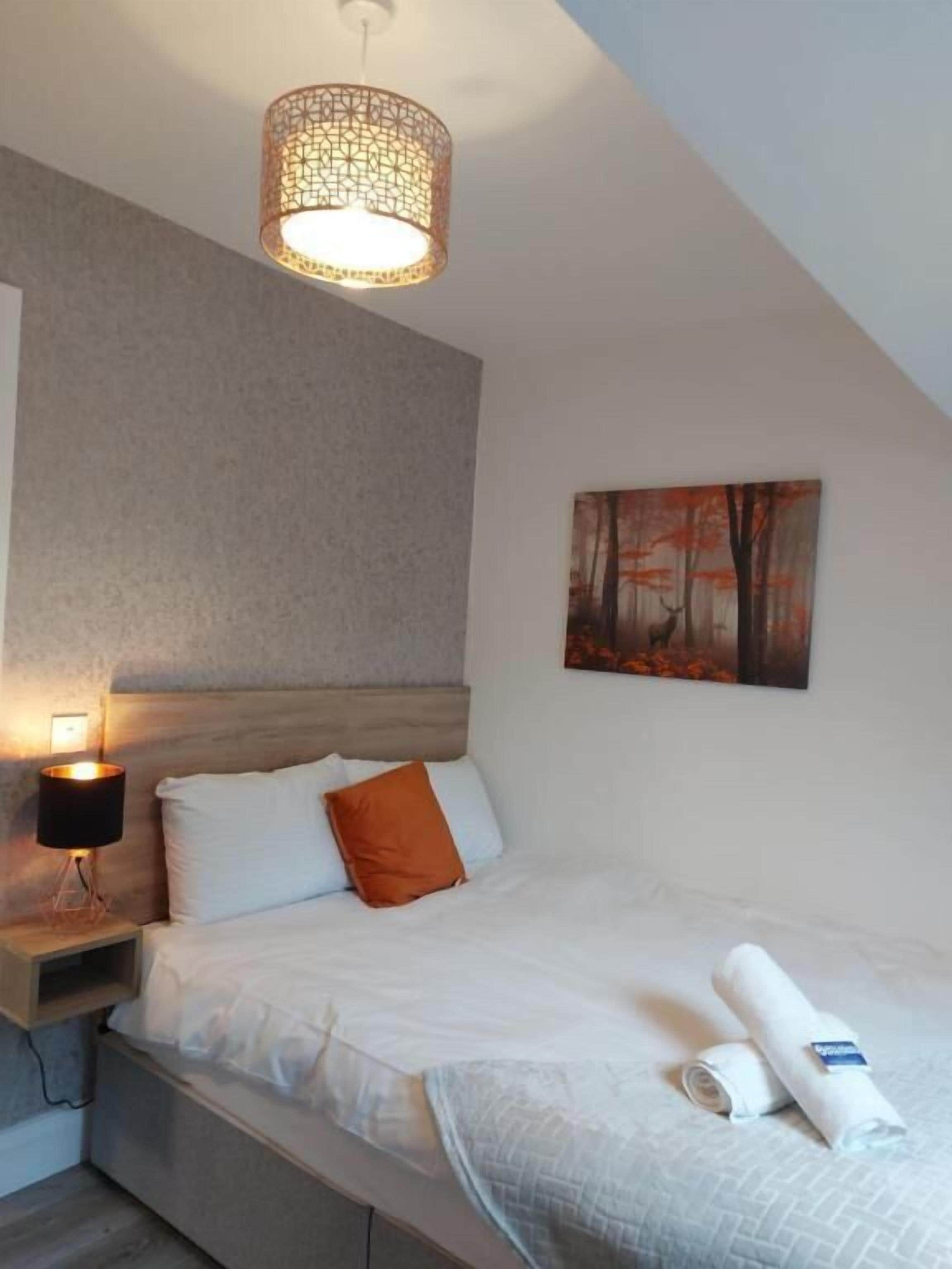 A bedroom with a bed, a nightstand, a wall-mounted lamp, and a painting.