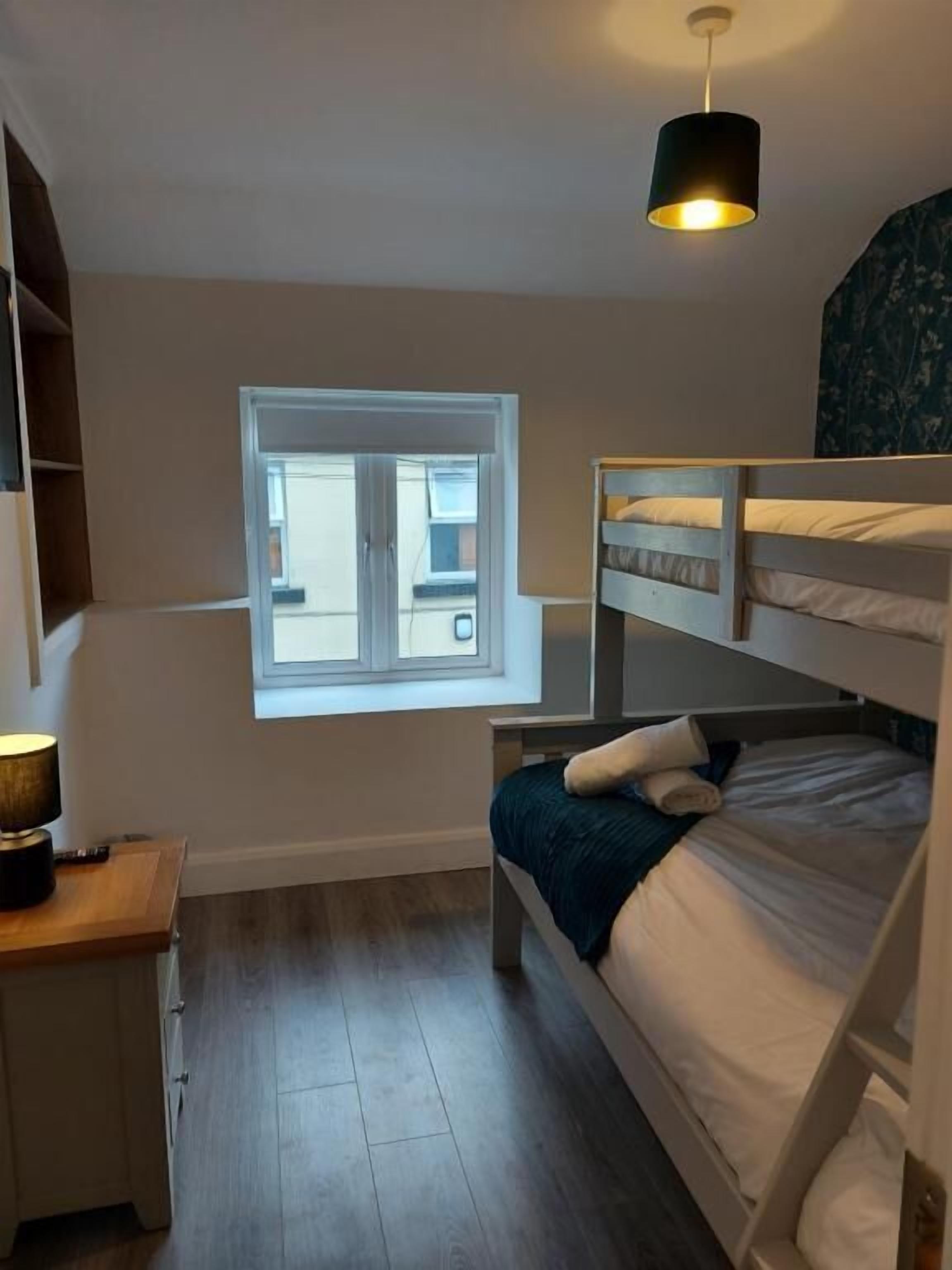 A small, well-lit room with a bunk bed, a desk with a lamp, and a window providing natural light.
