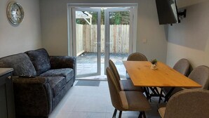 A modern living room with a sofa, dining table, chairs, a TV mounted on the wall, and a sliding glass door leading to an outdoor area. - 7 Eyre Square Lane (Galway)