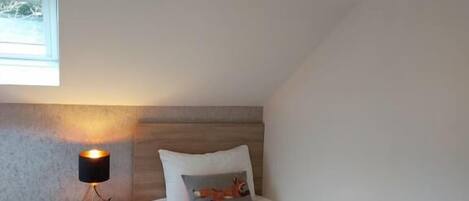 A bedroom with a bed, a nightstand, a lamp, and a window.