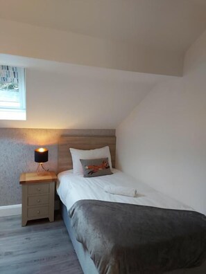 Une chambre à coucher avec un lit, une table de chevet, une lampe et une fenêtre.