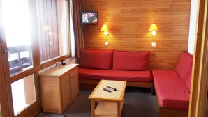 Ein gemütliches Zimmer mit einer Holzwand, einem Sofa, einem kleinen Tisch und einem über dem Sofa montierten Fernseher.
