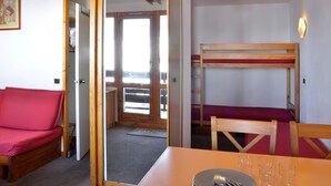 Ein Zimmer mit Etagenbett, einem Einzelbett, einem Tisch mit Gläsern und Besteck sowie einer Tür zu einem weiteren Raum.