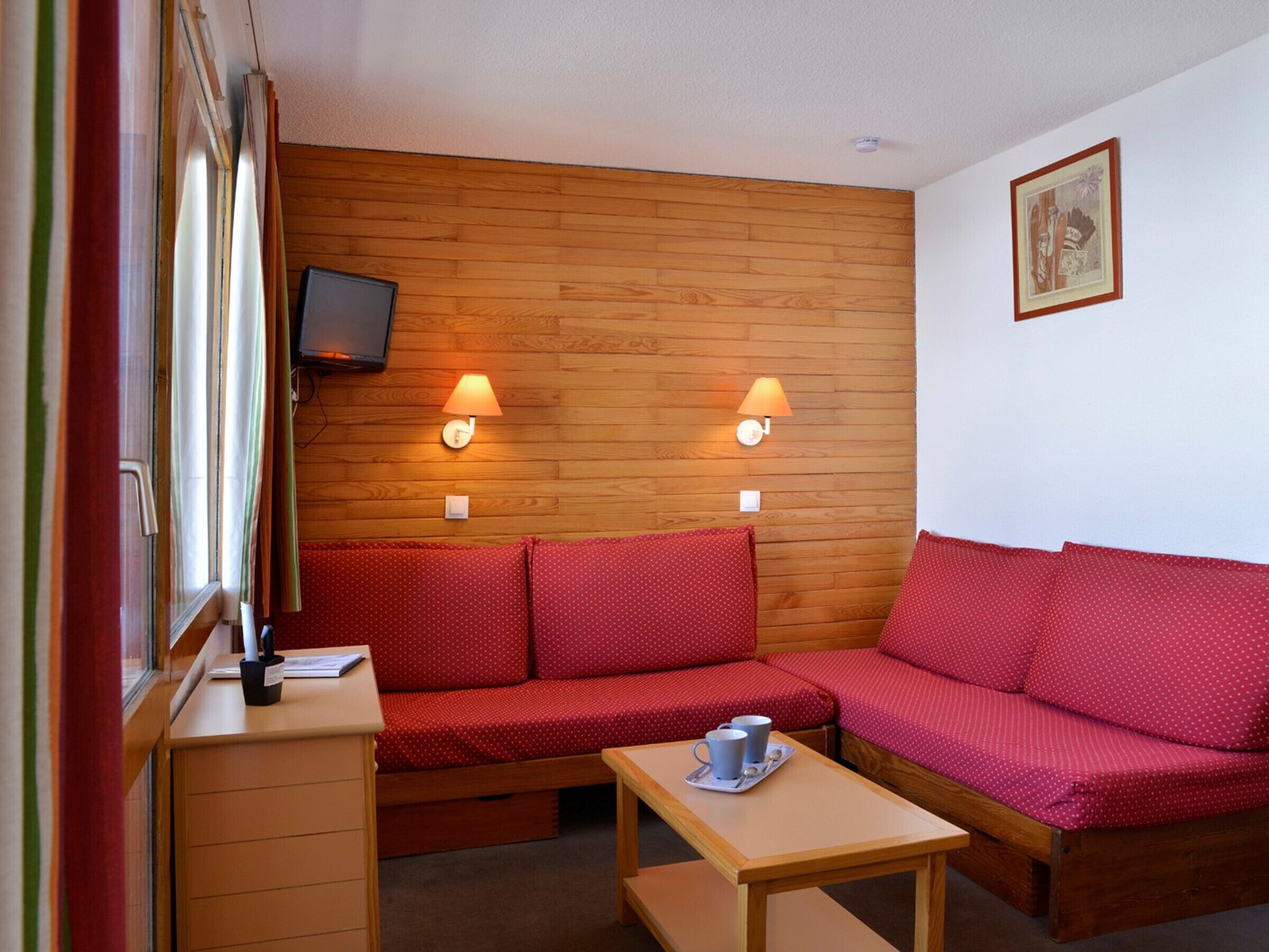 A cozy room with a wooden wall, a sofa, a table with cups, and a television on the wall.