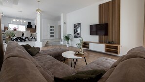 Ein modernes Wohnzimmer mit einer großen Eckcouch, einem runden Couchtisch und einem Flachbildfernseher, der an einer Holzvertäfelung angebracht ist.