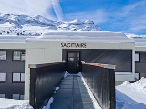 Entrada de um edifício com a placa 'SAGITTAIRE', e uma escadaria de metal que sobe.