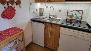 Une cuisine compacte avec des meubles en bois, un lave-vaisselle encastré et une machine à café posée sur le plan de travail.