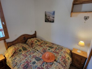 A single bed with a patterned bedspread, a small bedside table with a lamp, and a wall-mounted picture.