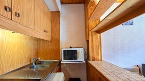 A compact kitchenette with wooden cabinets, a built-in microwave, and a small trash bin. - Comfortable studio in Flaine, balcony, near slopes (Flaine)
