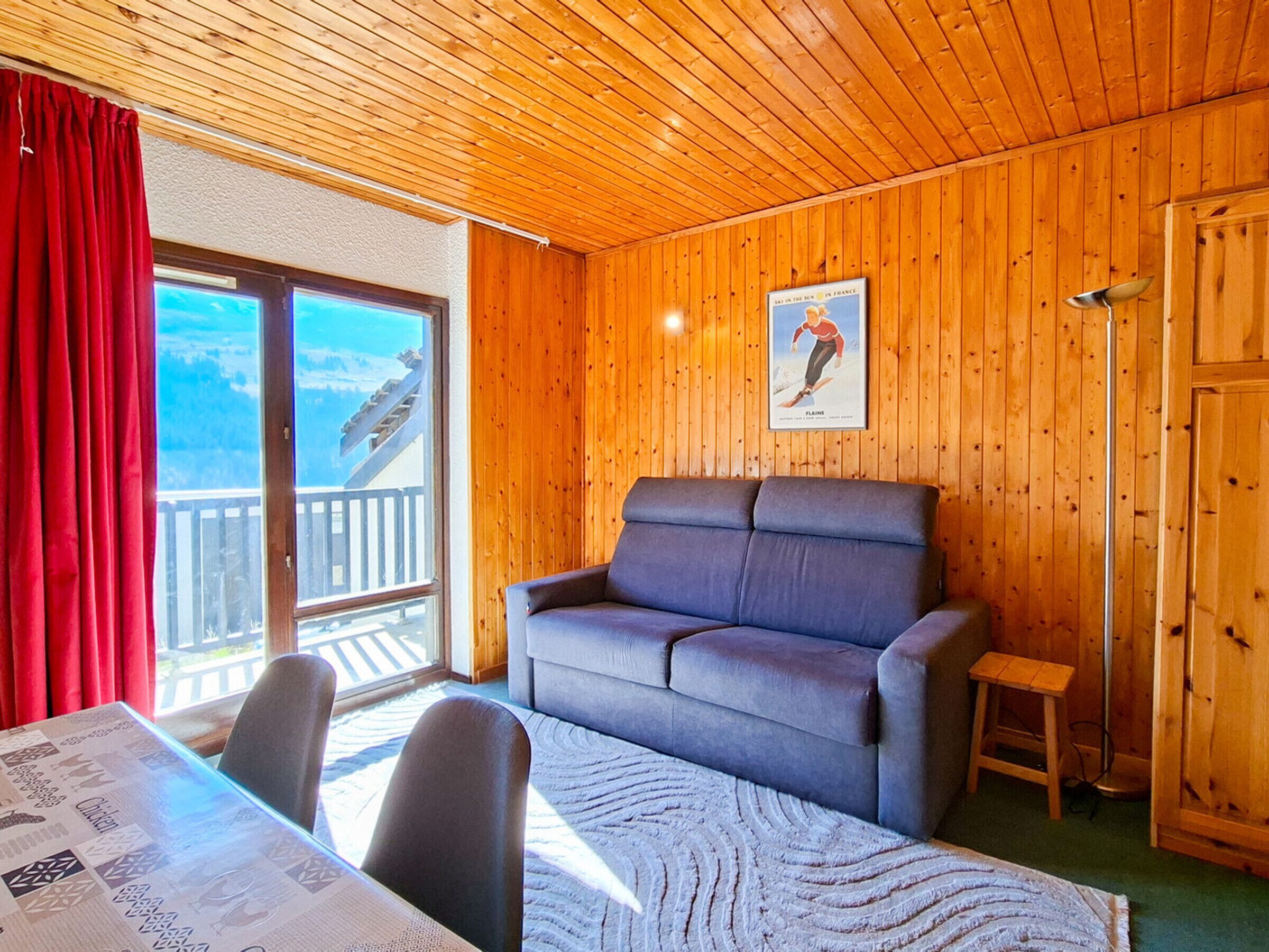 Una habitación acogedora con techo de madera, un sofá gris, un taburete pequeño de madera y una mesa con un periódico.
