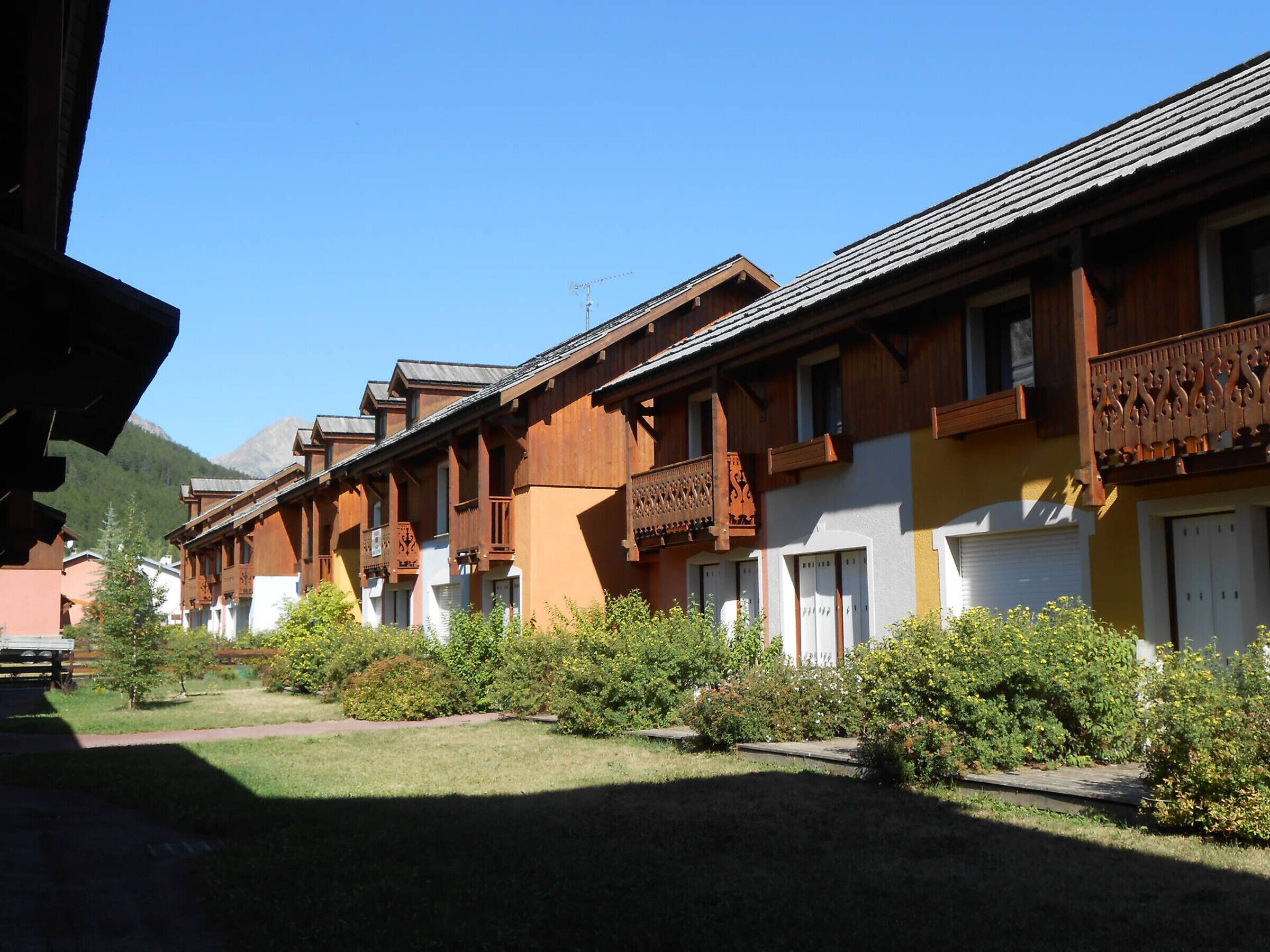 A row of wooden buildings with balconies, a clear sky, and a mountain in the background.