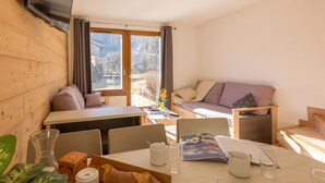 Une pièce chaleureuse avec un mur en bois, un canapé, une table à manger avec des chaises et un téléviseur fixé au mur.