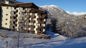 Un immeuble à plusieurs étages doté de balcons, se dressant sur fond de montagnes enneigées.
