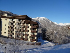 A multi-story building with balconies, set against a snowy mountain backdrop. - Studio 4 ppl, shuttle to slopes, outdoor parking (Saint-Chaffrey)