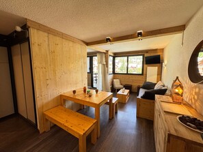 A cozy cabin interior with wooden walls and floors, a dining area with benches, a sofa, and a small table with a lamp. - Studio 4 ppl, shuttle to slopes, outdoor parking (Saint-Chaffrey)
