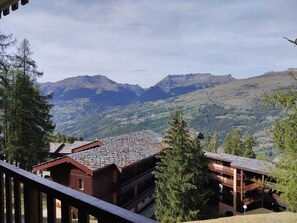 A mountain lodge with multiple floors and a stone roof, surrounded by forested hills and mountains. - Comfortable apartment with free parking in La Plagne (La Plagne Montchavin Les Coches)