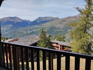 Vista da montanha com varanda de madeira, dando para um vale e montanhas ao longe.