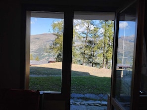 Ein Zimmer mit großem Fenster und Blick auf eine grüne Parklandschaft mit Bäumen und einem entfernten Berg.