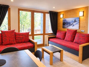 A modern interior with a wooden sofa set, a dining table, and a view through large windows. - Comfortable apartment, near slopes, terrace, pets allowed (La Plagne Montchavin Les Coches)