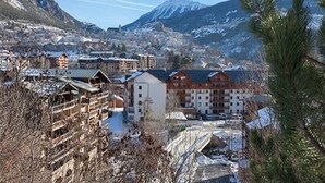 Un pueblo montañoso con edificios, incluyendo un hotel de varios pisos y un telesilla.