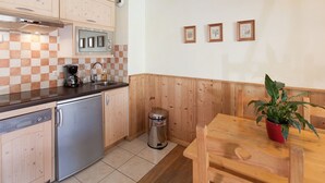Cocina funcional con lavavajillas, cafetera y contenedor de basura. Hay una mesa de madera con una planta en maceta.