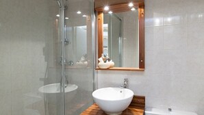 Un baño moderno con cabina de ducha de vidrio, tocador de madera con lavamanos blanco y un espejo grande sobre el tocador.